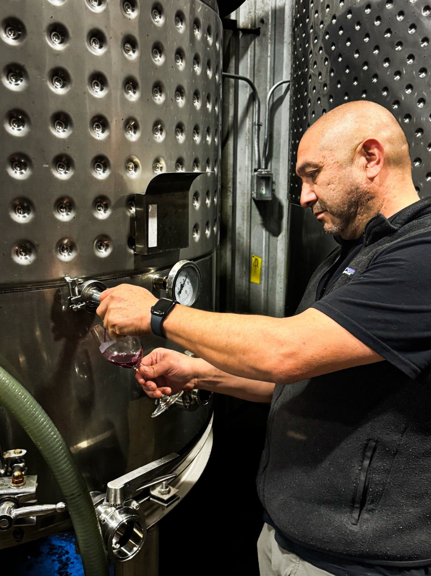 Man sampling wine from a large metal tank